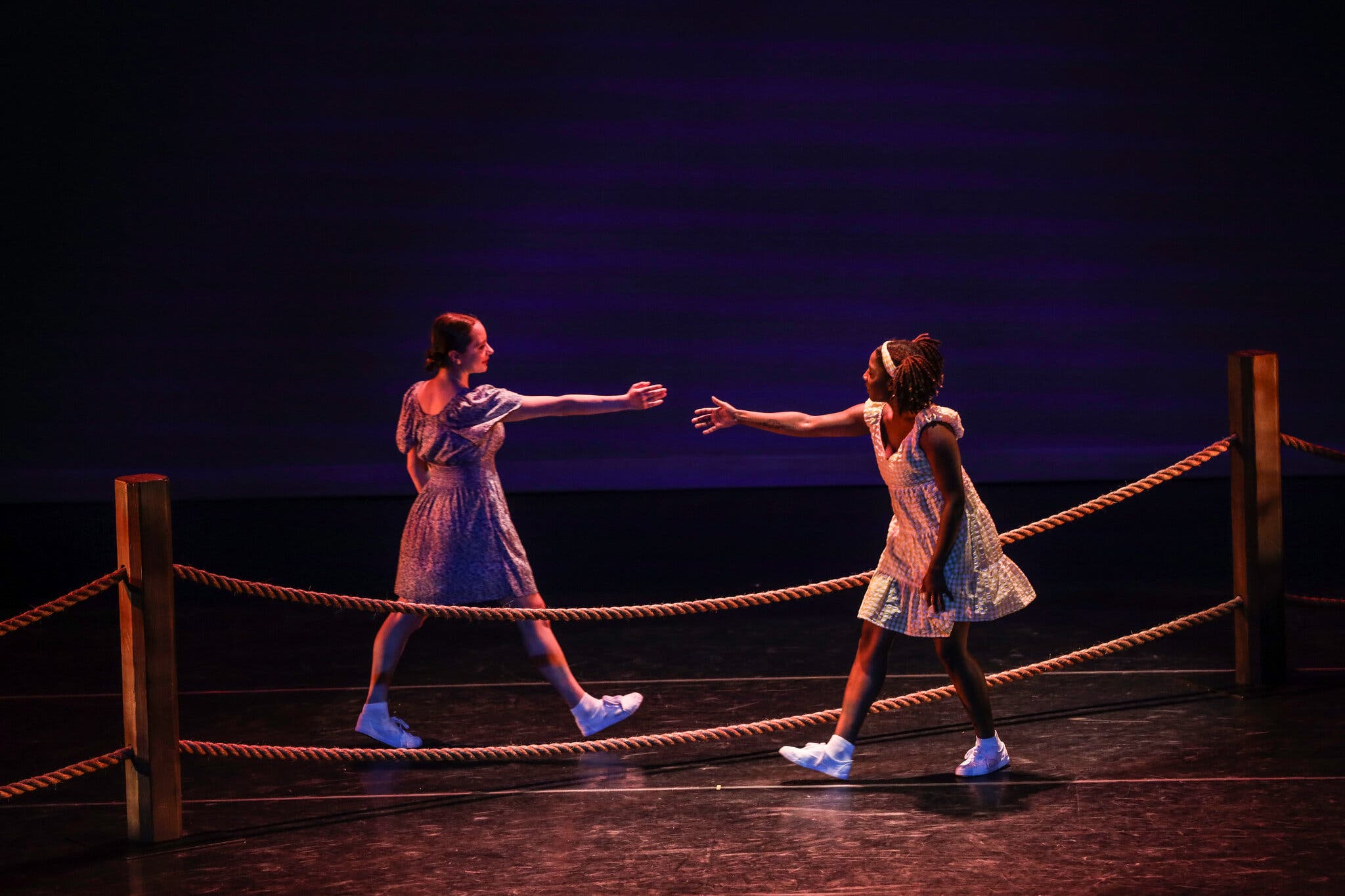 Two girls, one White and one African-American, shake hands over a low fence as they greet each other.