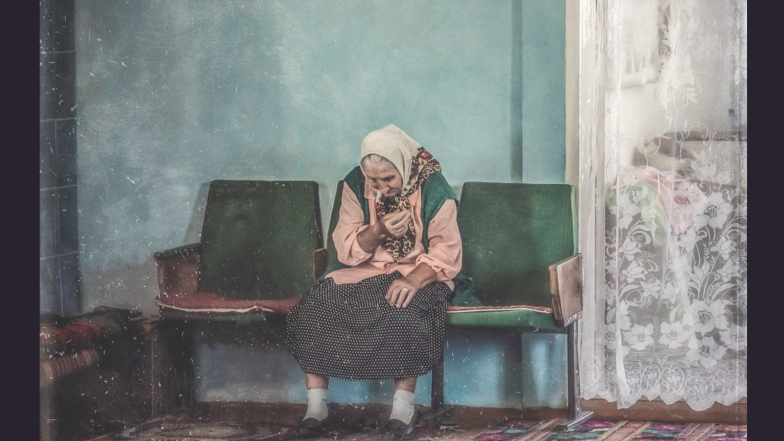 photo of an old white Ukrainian woman in a white headscarf sitting in a chair