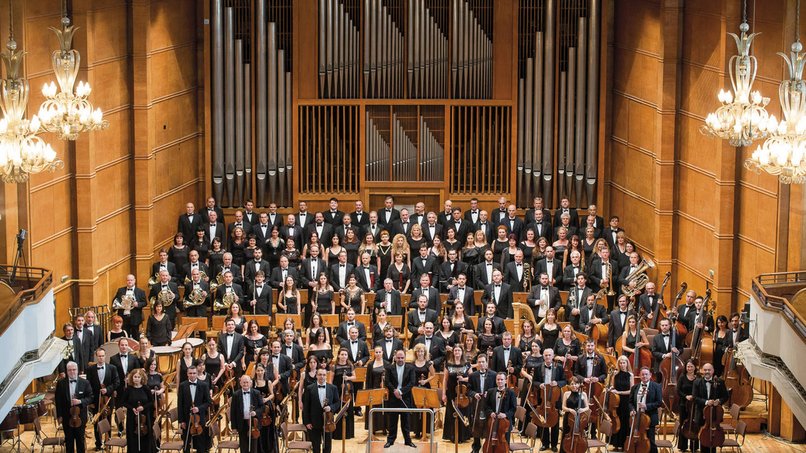 an orchestra stands for a formal portrait on a grand stage