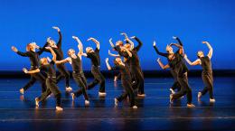 Dancers wearing all black on stage against a blue backdrop