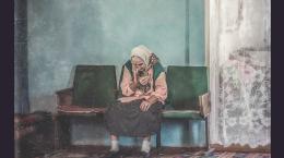 photo of an old white Ukrainian woman in a white headscarf sitting in a chair