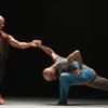 Two black male dancers in loose dance wear pose onstage