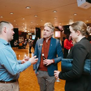 Two men and a woman holding drinks and chatting in Krannert Center Lobby