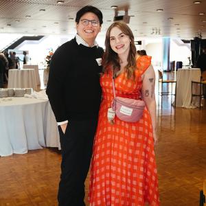 Man in black sweater and woman in reddish orange dress smile for camera
