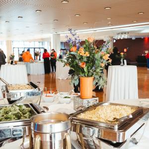 buffet table with chafing dishes of pasta and broccoli and a centerpiece of fresh flowers