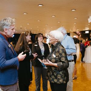 A man in a blue blazer chats with a woman holding a glass of wine