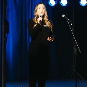 Bethany Whoric, associate director of advancement for Krannert Center, wearing a black dress, speaks into a microphone on stage